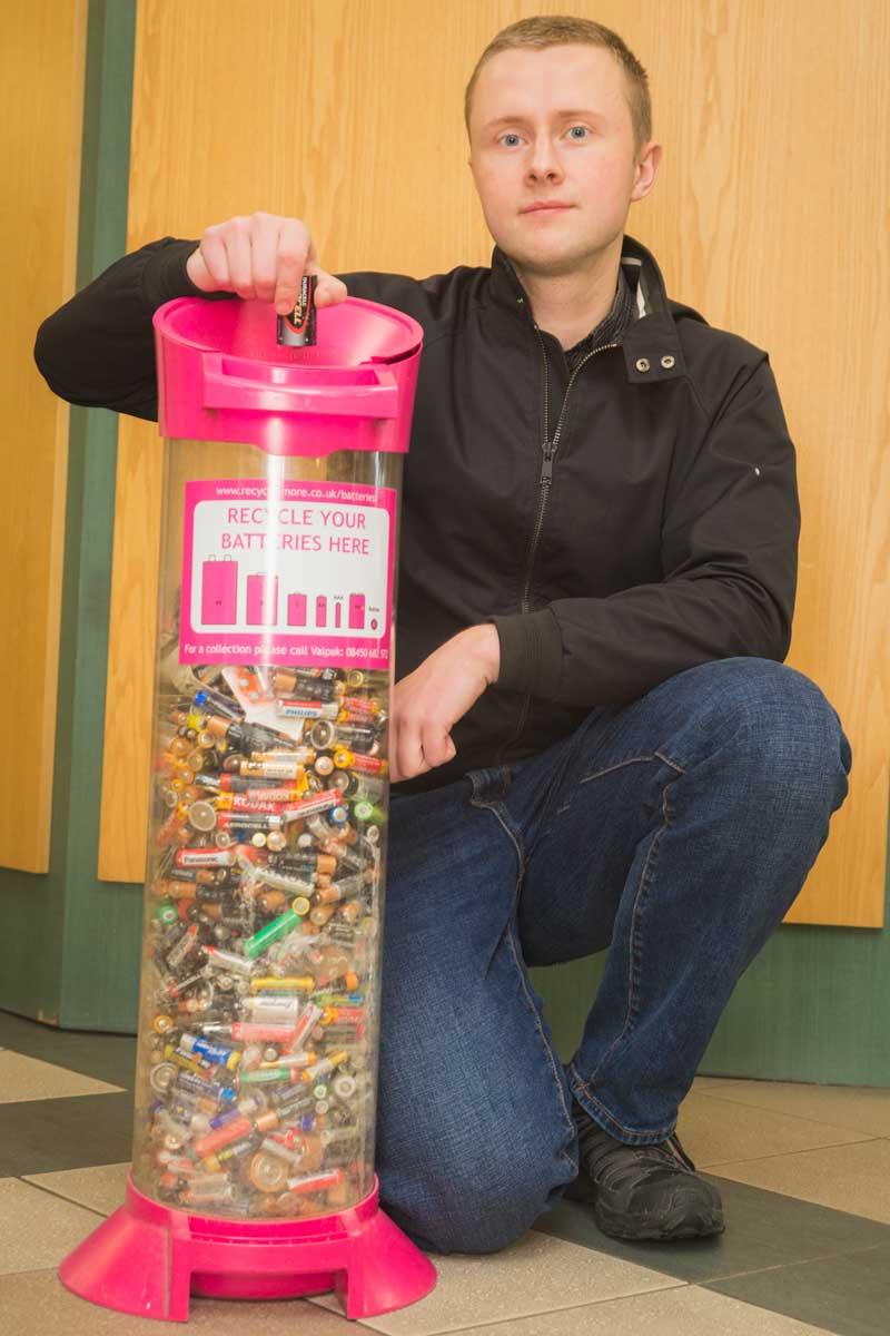 Person standing next to a battery recycling container