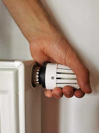 Person with their hand on a radiator thermostat